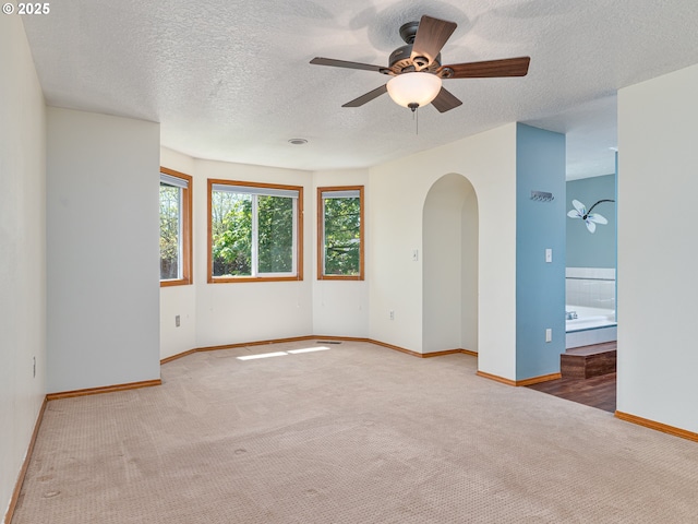 carpeted empty room featuring arched walkways, ceiling fan, baseboards, and a textured ceiling