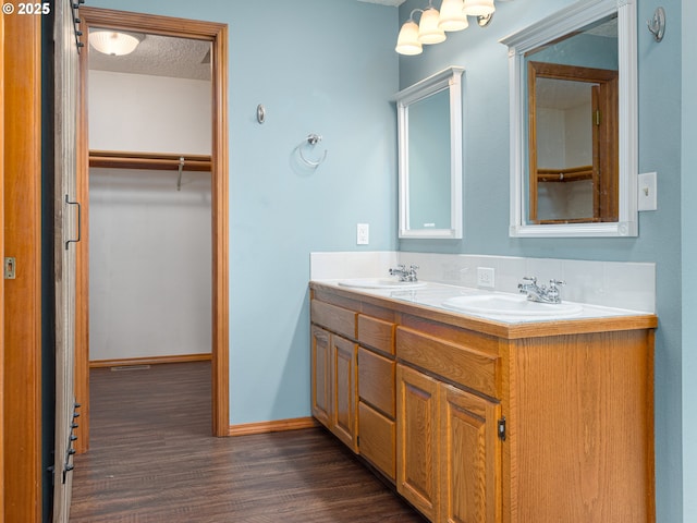 bathroom featuring double vanity, a walk in closet, wood finished floors, a sink, and baseboards