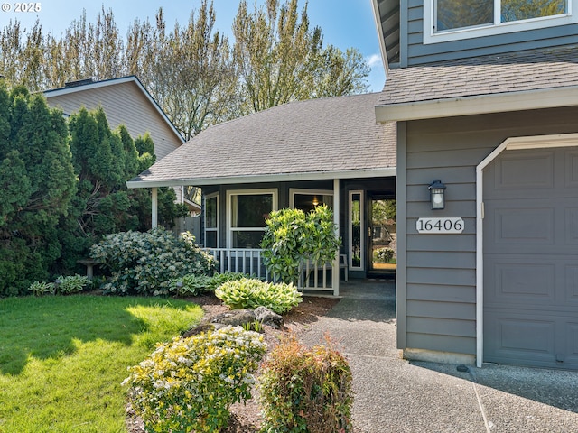 doorway to property with a garage, a shingled roof, and a lawn