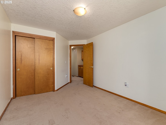 unfurnished bedroom featuring a closet, a textured ceiling, baseboards, and light colored carpet