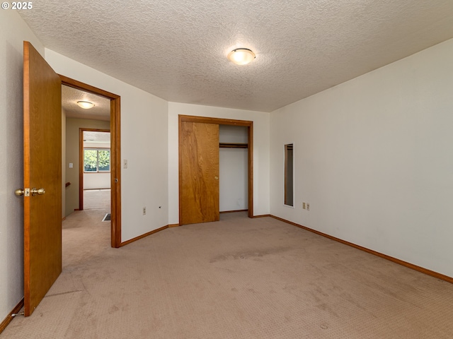 unfurnished bedroom featuring light colored carpet, a textured ceiling, baseboards, and a closet
