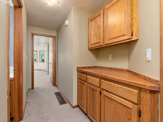 hall featuring light colored carpet, a textured ceiling, visible vents, and baseboards