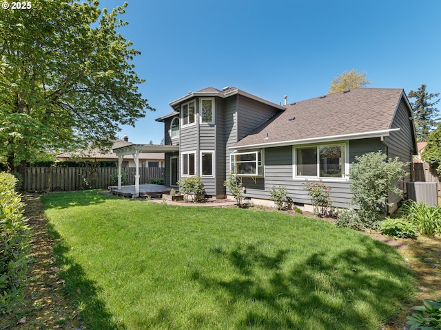 rear view of property featuring fence, a shingled roof, a patio area, central air condition unit, and a yard