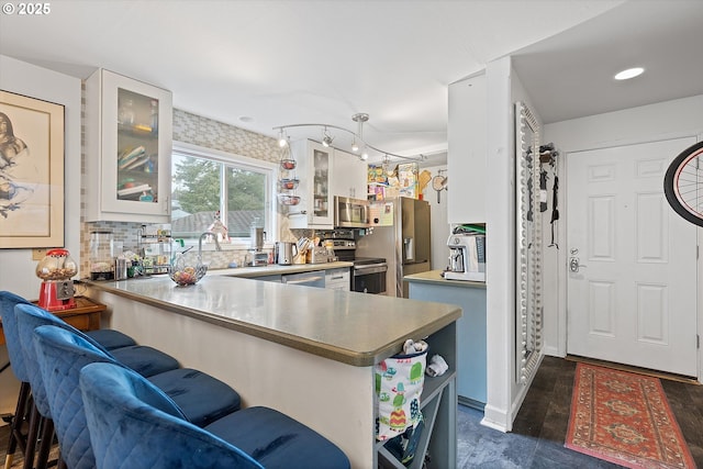 kitchen with white cabinetry, stainless steel appliances, a kitchen bar, decorative backsplash, and kitchen peninsula