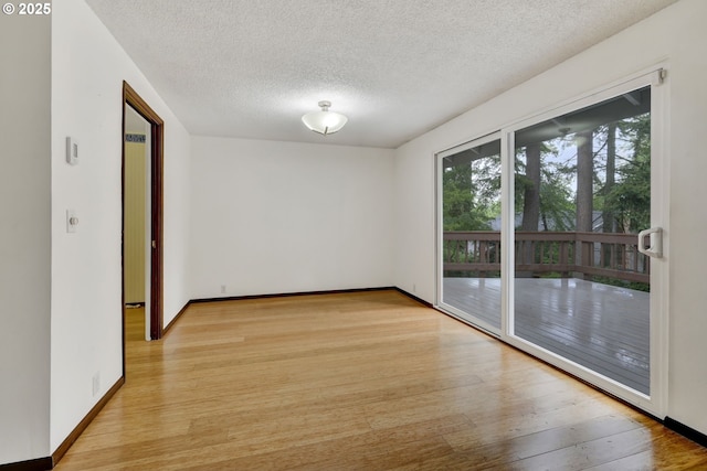empty room with light wood-style floors, a textured ceiling, and baseboards