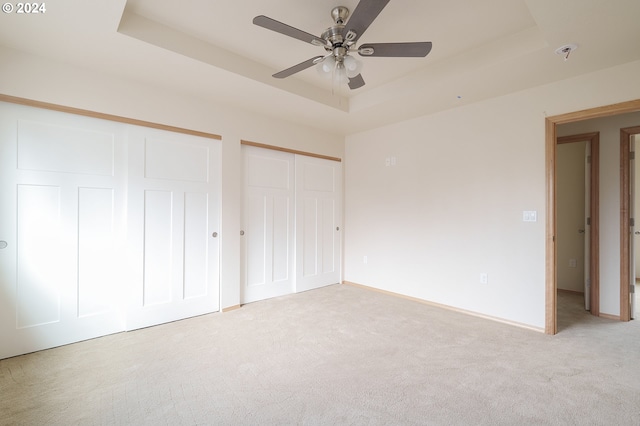 unfurnished bedroom featuring a raised ceiling, multiple closets, light colored carpet, and ceiling fan