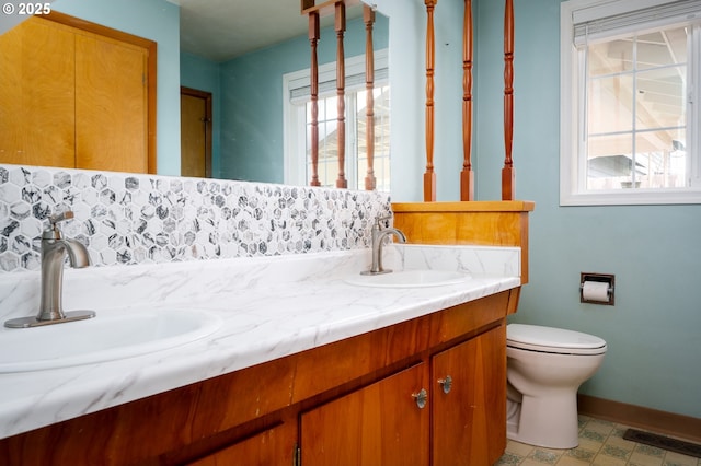 full bathroom with double vanity, a sink, toilet, and baseboards