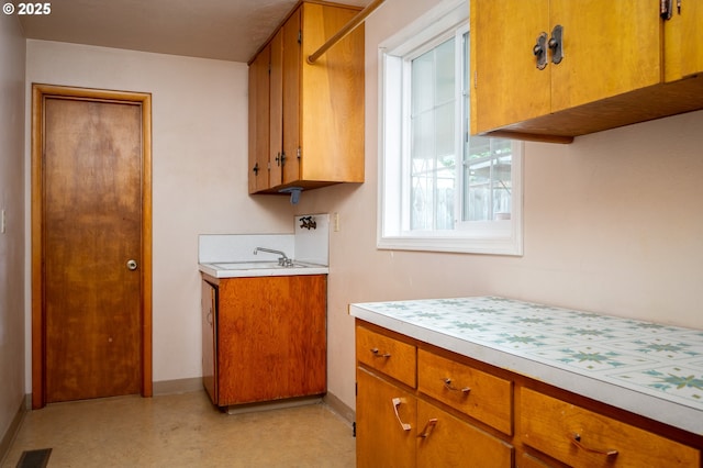 kitchen with brown cabinetry, light countertops, visible vents, and baseboards