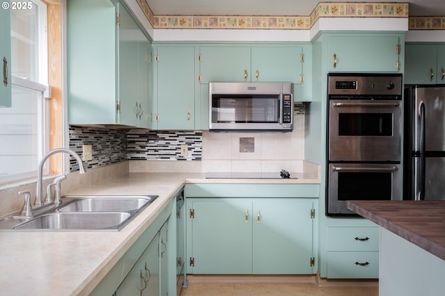 kitchen featuring stainless steel appliances, light countertops, a sink, and decorative backsplash