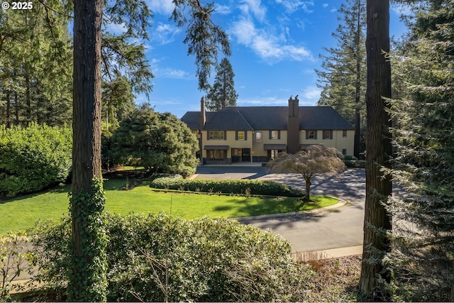 rear view of property featuring a lawn, a chimney, and driveway