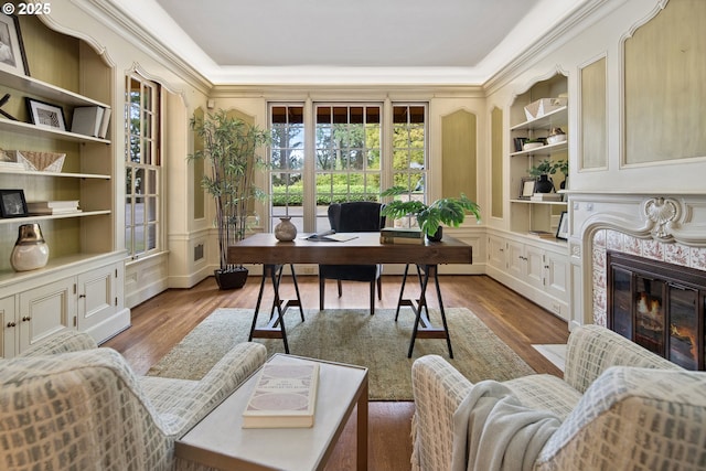 office with built in shelves, wood finished floors, a high end fireplace, and a decorative wall