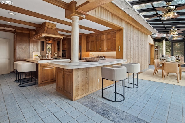 kitchen with beamed ceiling, a kitchen bar, a ceiling fan, light countertops, and ornate columns