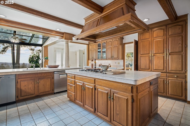 kitchen with a center island, beamed ceiling, light countertops, brown cabinets, and stainless steel dishwasher