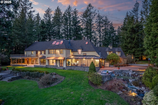 back of house at dusk featuring a standing seam roof, a yard, metal roof, a chimney, and a patio area