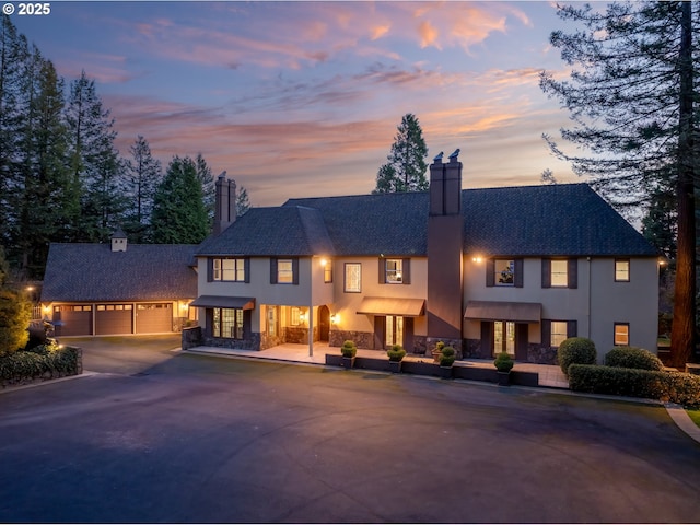 view of front of property featuring driveway, stucco siding, a chimney, an outdoor structure, and a garage