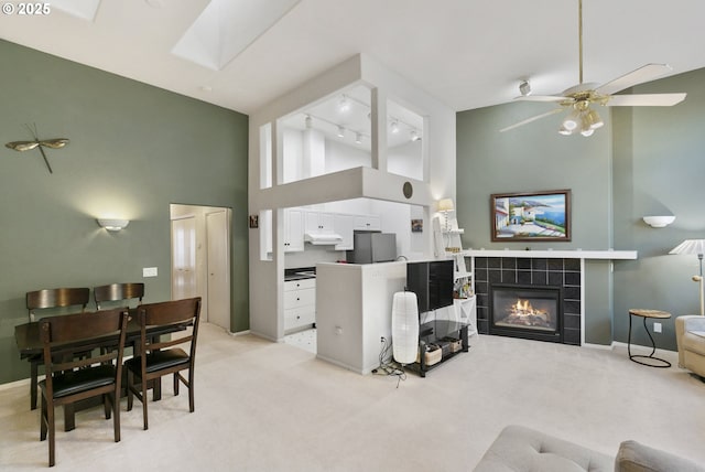 carpeted living room with a skylight, a tile fireplace, rail lighting, and a high ceiling