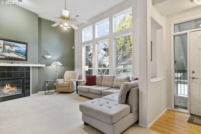 living room featuring a tiled fireplace, a high ceiling, ceiling fan, and light wood-type flooring