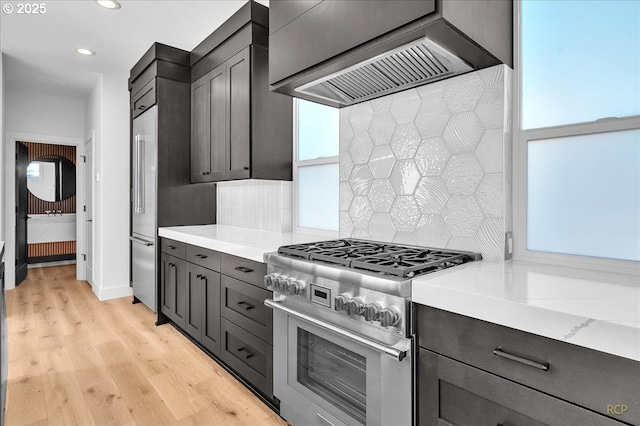 kitchen with decorative backsplash, high end range, light wood-type flooring, and custom exhaust hood