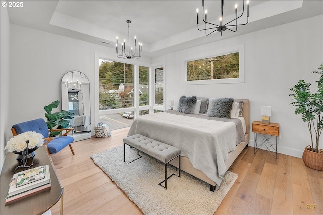 bedroom with a raised ceiling, a notable chandelier, and hardwood / wood-style flooring