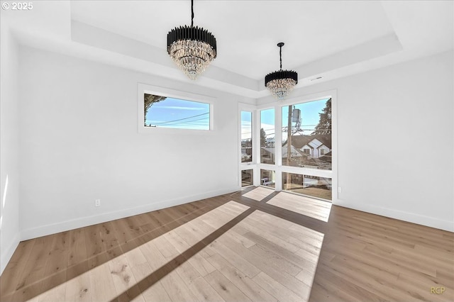 unfurnished dining area featuring a tray ceiling, light wood-type flooring, and an inviting chandelier