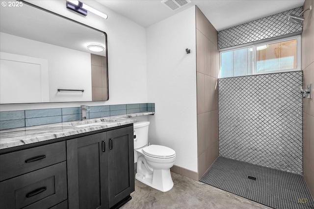 bathroom with toilet, vanity, a tile shower, and concrete flooring