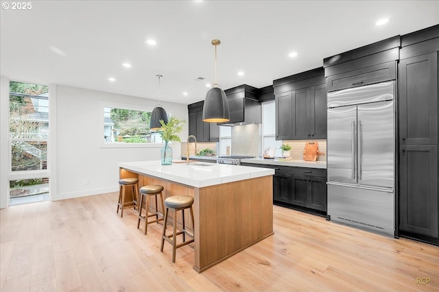 kitchen featuring light hardwood / wood-style floors, hanging light fixtures, stainless steel built in refrigerator, and a center island with sink