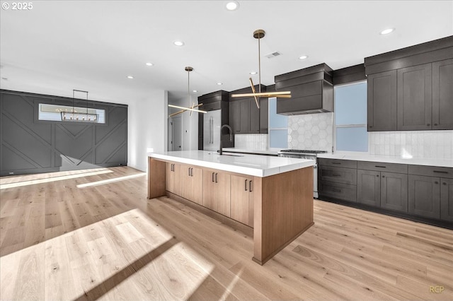 kitchen featuring decorative light fixtures, a center island with sink, high end stove, light wood-type flooring, and custom range hood