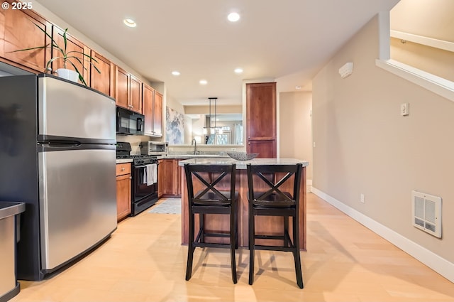 kitchen featuring a kitchen island, pendant lighting, a kitchen bar, black appliances, and light stone countertops