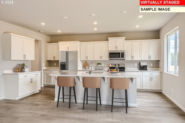 kitchen with sink, a breakfast bar, a kitchen island with sink, stainless steel appliances, and white cabinets