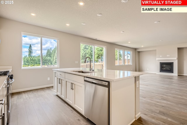 kitchen featuring sink, appliances with stainless steel finishes, light hardwood / wood-style floors, white cabinets, and a center island with sink