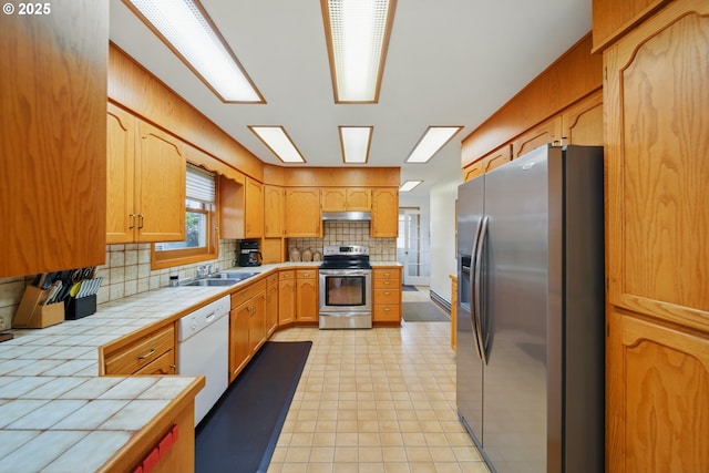 113 NE 7th Ave, Milton-Freewater, OR 97862 - kitchen featuring appliances with stainless steel finishes, tile counters, tasteful backsplash, under cabinet range hood, and a sink