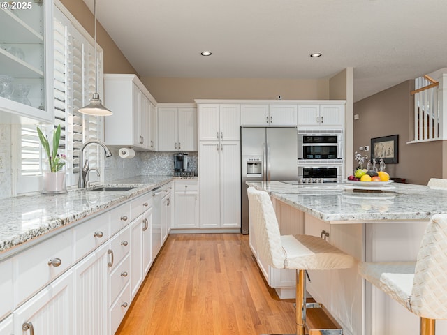 8833 SE Bristol Park Dr, Happy Valley, OR 97086 - kitchen featuring appliances with stainless steel finishes, light wood-style floors, white cabinetry, glass insert cabinets, and a breakfast bar