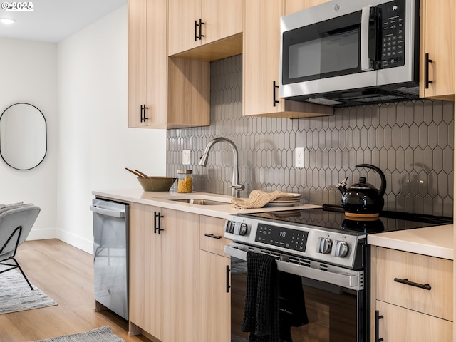 kitchen with light countertops, light brown cabinets, appliances with stainless steel finishes, and a sink