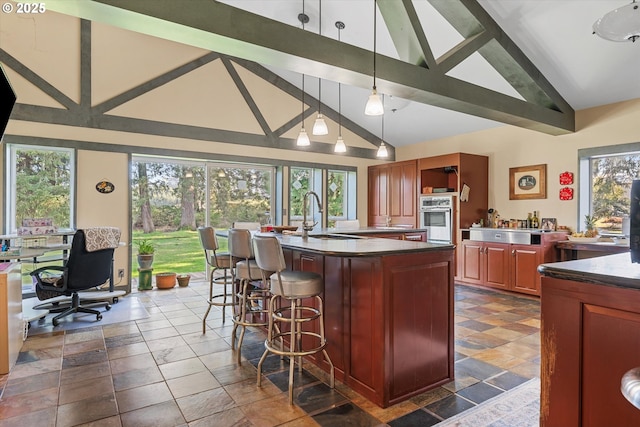 kitchen with sink, a breakfast bar area, oven, hanging light fixtures, and beam ceiling