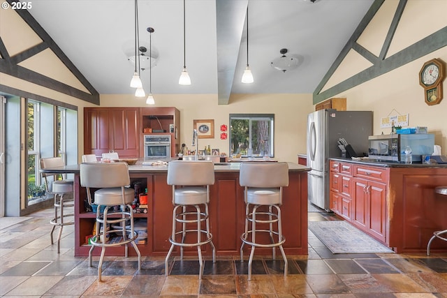 kitchen featuring appliances with stainless steel finishes, a kitchen breakfast bar, a center island, decorative light fixtures, and vaulted ceiling