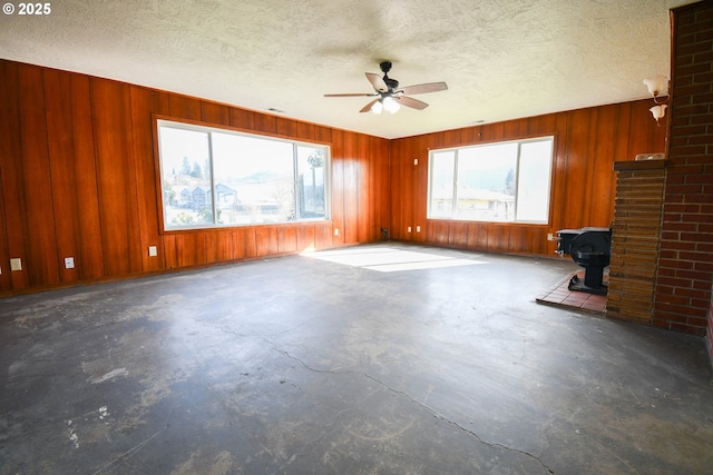 151 NW Sherry St, Winston, OR 97496 - unfurnished living room featuring ceiling fan, wooden walls, a textured ceiling, and a wood stove