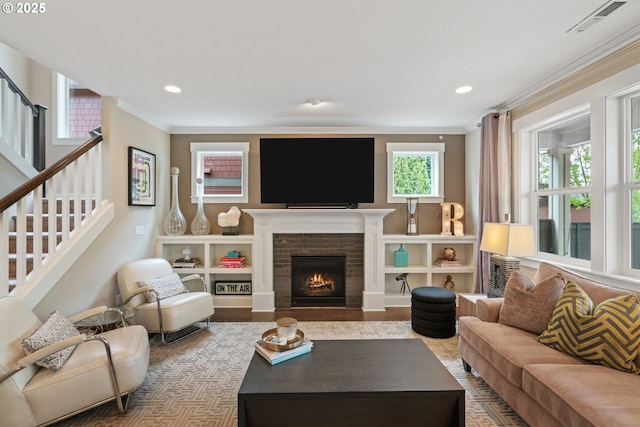 living room with a brick fireplace, recessed lighting, visible vents, ornamental molding, and stairway