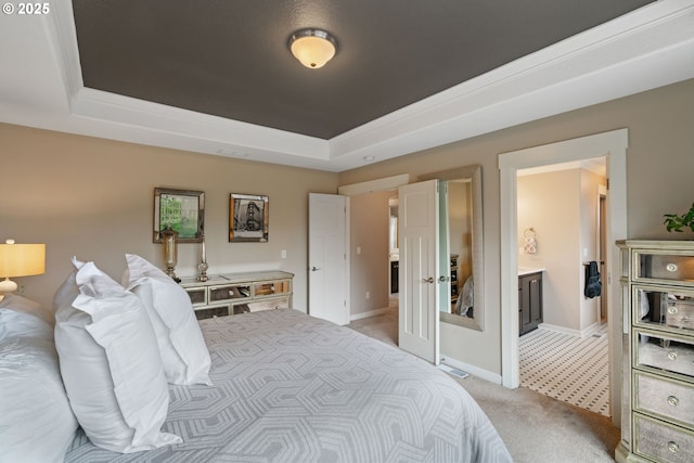 bedroom featuring baseboards, a raised ceiling, ensuite bath, and light carpet