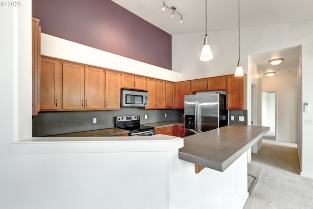 kitchen featuring appliances with stainless steel finishes, a peninsula, a high ceiling, tile countertops, and a breakfast bar