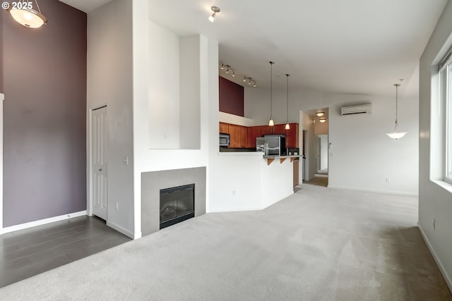 unfurnished living room with a wall unit AC, rail lighting, baseboards, carpet flooring, and a tile fireplace