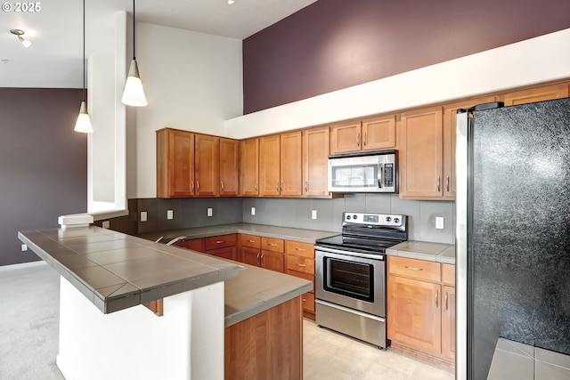 kitchen featuring appliances with stainless steel finishes, a peninsula, a high ceiling, tile countertops, and a kitchen breakfast bar