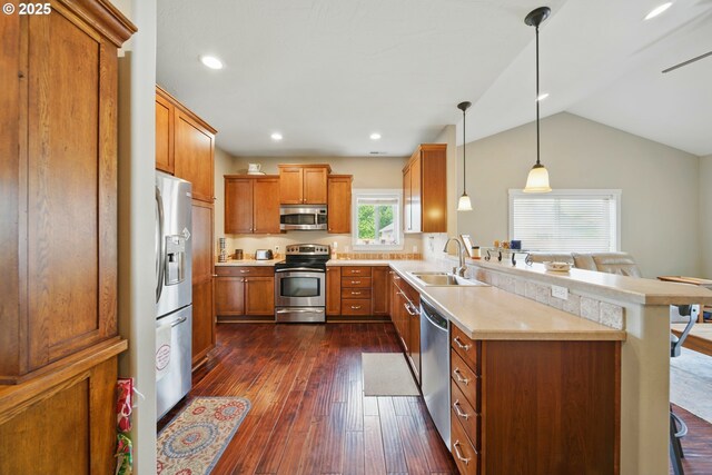 kitchen featuring brown cabinetry, dark wood-style flooring, appliances with stainless steel finishes, a sink, and a peninsula
