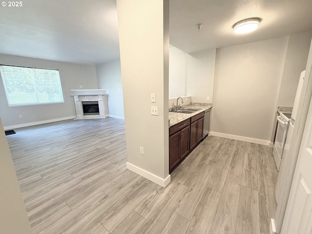 kitchen with light wood-style flooring, a sink, baseboards, dark brown cabinets, and a glass covered fireplace