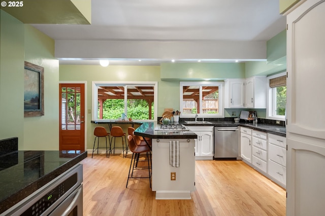 6116 SE 36th Ave, Portland, OR 97202 - kitchen featuring appliances with stainless steel finishes, light wood-style floors, a sink, white cabinetry, and a kitchen breakfast bar