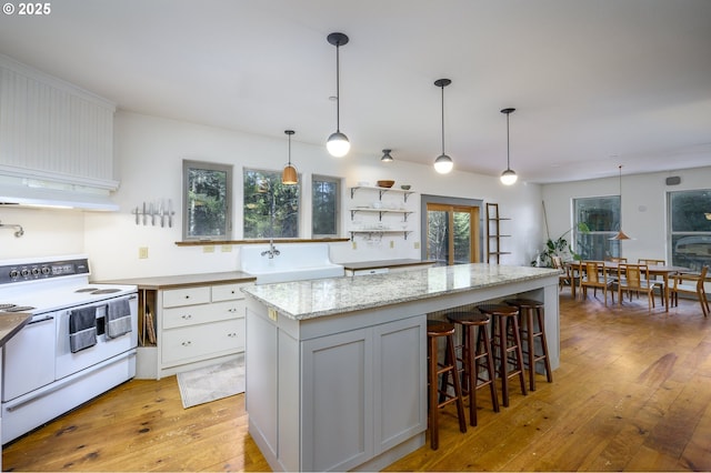 kitchen featuring light stone counters, light hardwood / wood-style flooring, pendant lighting, white range with electric cooktop, and white cabinets