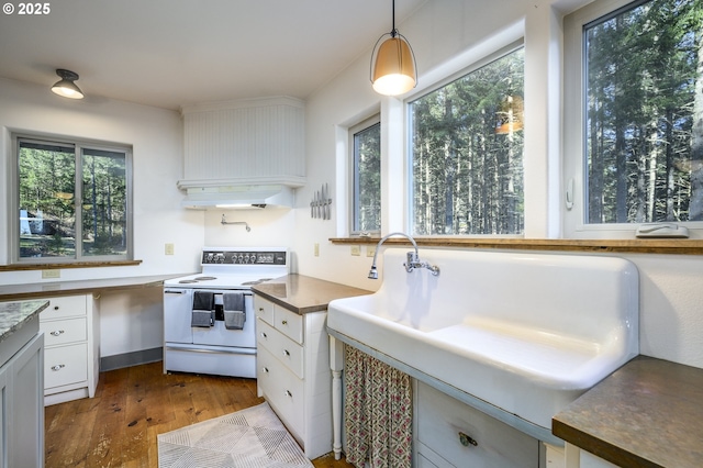 kitchen with hardwood / wood-style floors, white range with electric stovetop, decorative light fixtures, ventilation hood, and white cabinetry