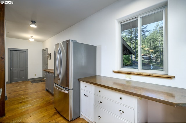 kitchen featuring stainless steel refrigerator, white cabinetry, built in desk, and light hardwood / wood-style flooring