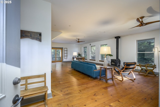 living room with ceiling fan, a wood stove, and light hardwood / wood-style floors