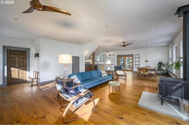 living room featuring wood-type flooring, ceiling fan, and a wood stove