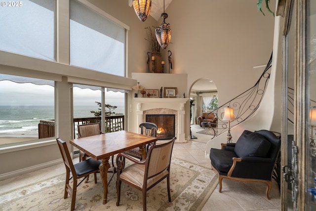 tiled dining space featuring a high end fireplace, high vaulted ceiling, a healthy amount of sunlight, and a water view